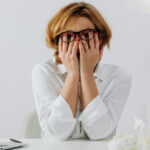 Femme au bureau, les mains sur les yeux, submergée par le stress et la surcharge de travail : l'importance d'une formation stress au travail